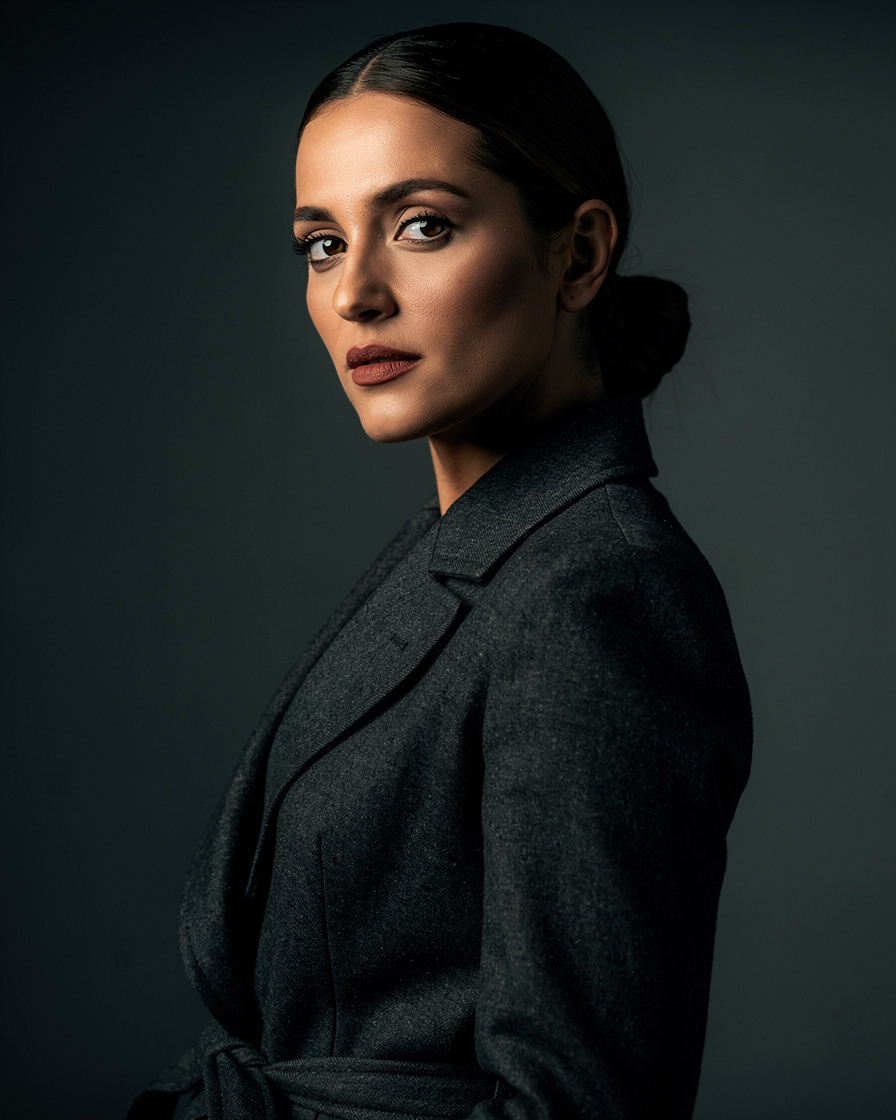 Elegant Argentine actress in a tailored dark coat looking off camera in dramatic studio light